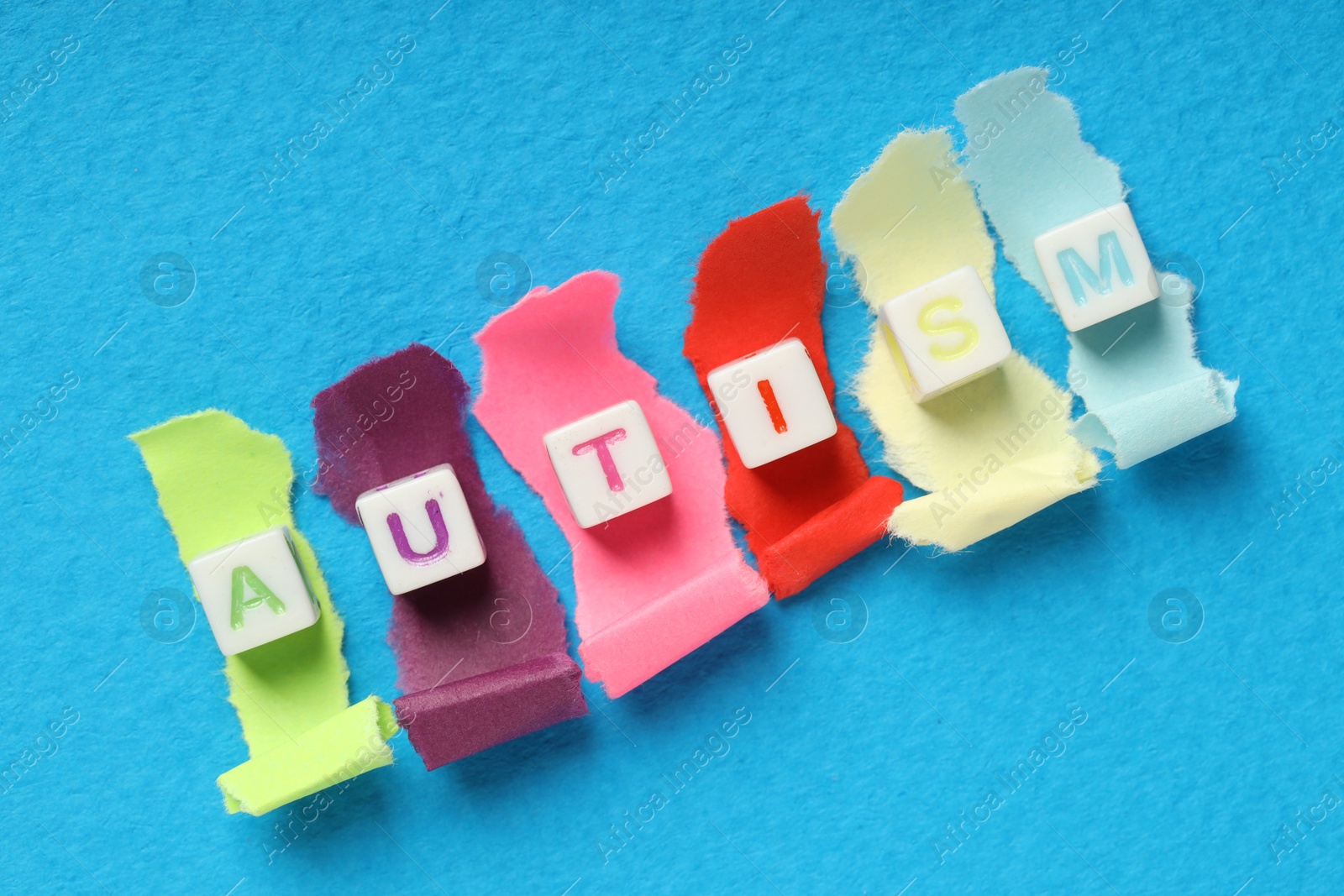 Photo of Word Autism made with cubes and cut colorful paper on light blue background, flat lay