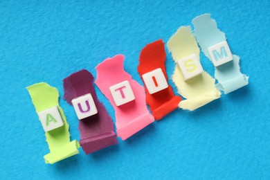 Photo of Word Autism made with cubes and cut colorful paper on light blue background, flat lay