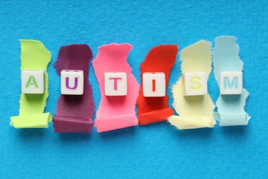 Photo of Word Autism made with cubes and cut colorful paper on light blue background, flat lay