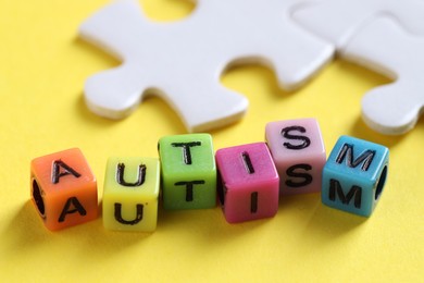 Photo of Word Autism made with colorful cubes and puzzle pieces on yellow background, closeup