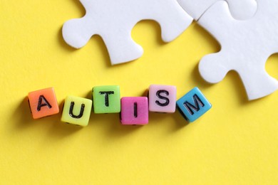 Photo of Word Autism made with colorful cubes and puzzle pieces on yellow background, flat lay