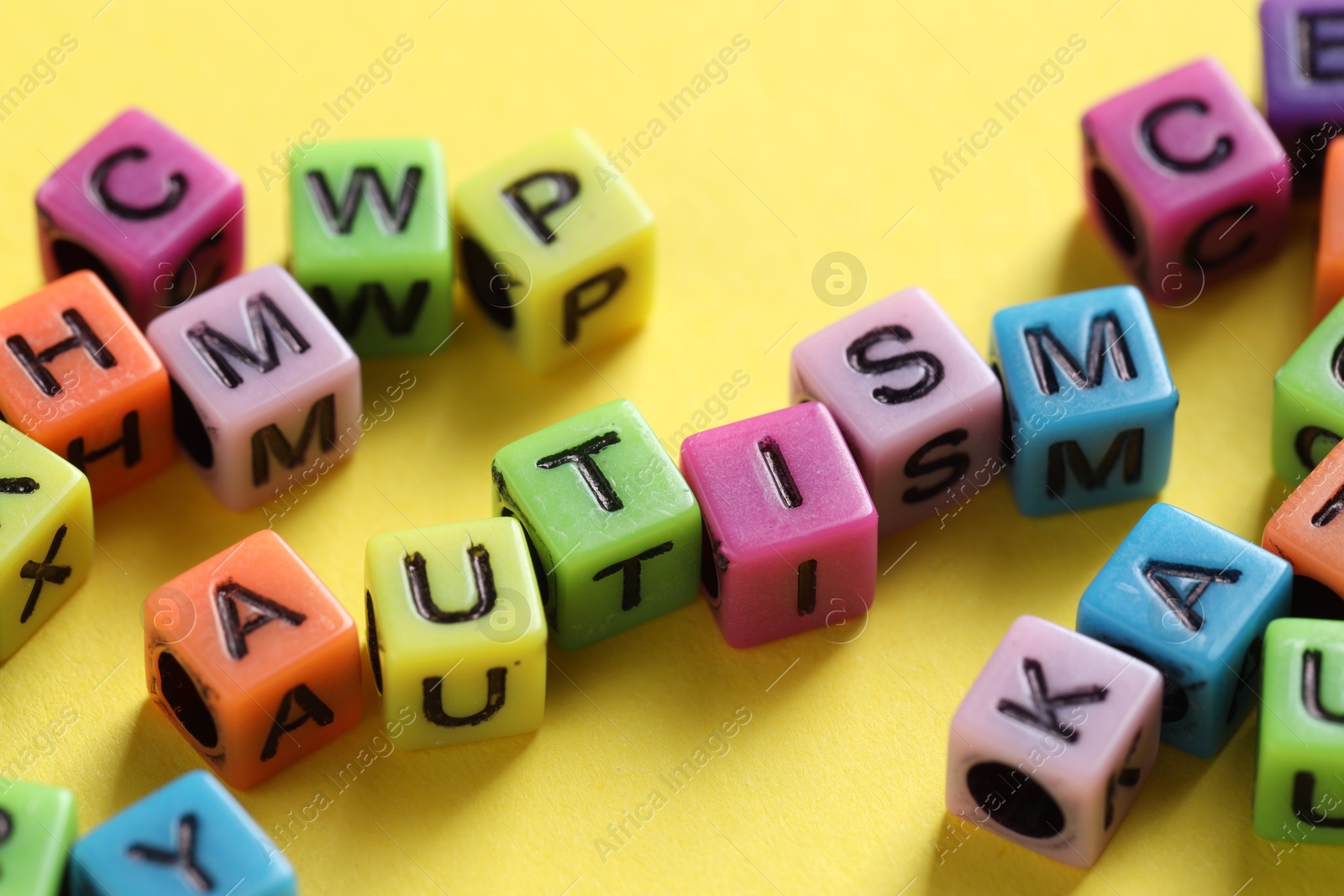 Photo of Word Autism made with colorful cubes on yellow background, closeup