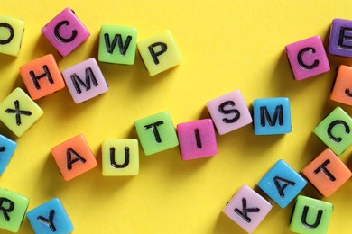 Photo of Word Autism made with colorful cubes on yellow background, flat lay