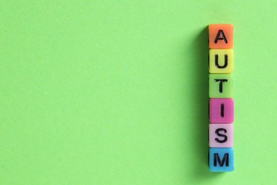 Photo of Word Autism made with colorful cubes on green background, flat lay. Space for text