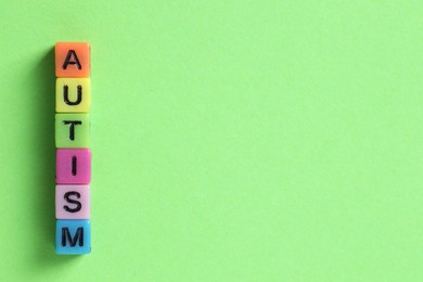 Photo of Word Autism made with colorful cubes on green background, flat lay. Space for text