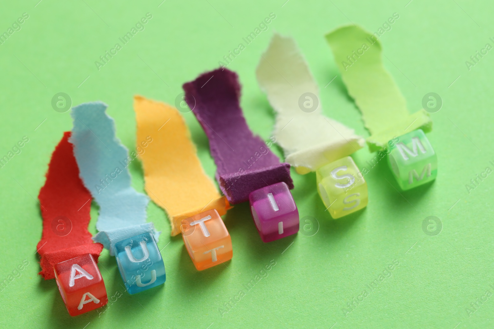 Photo of Word Autism made with cubes and cut colorful paper on green background, closeup