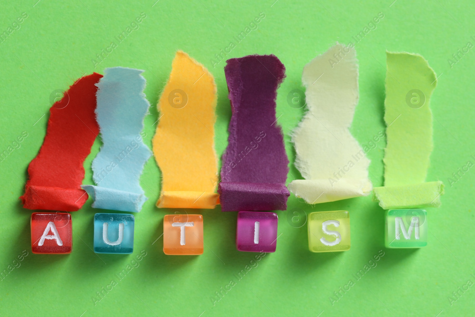 Photo of Word Autism made with cubes and cut colorful paper on green background, flat lay