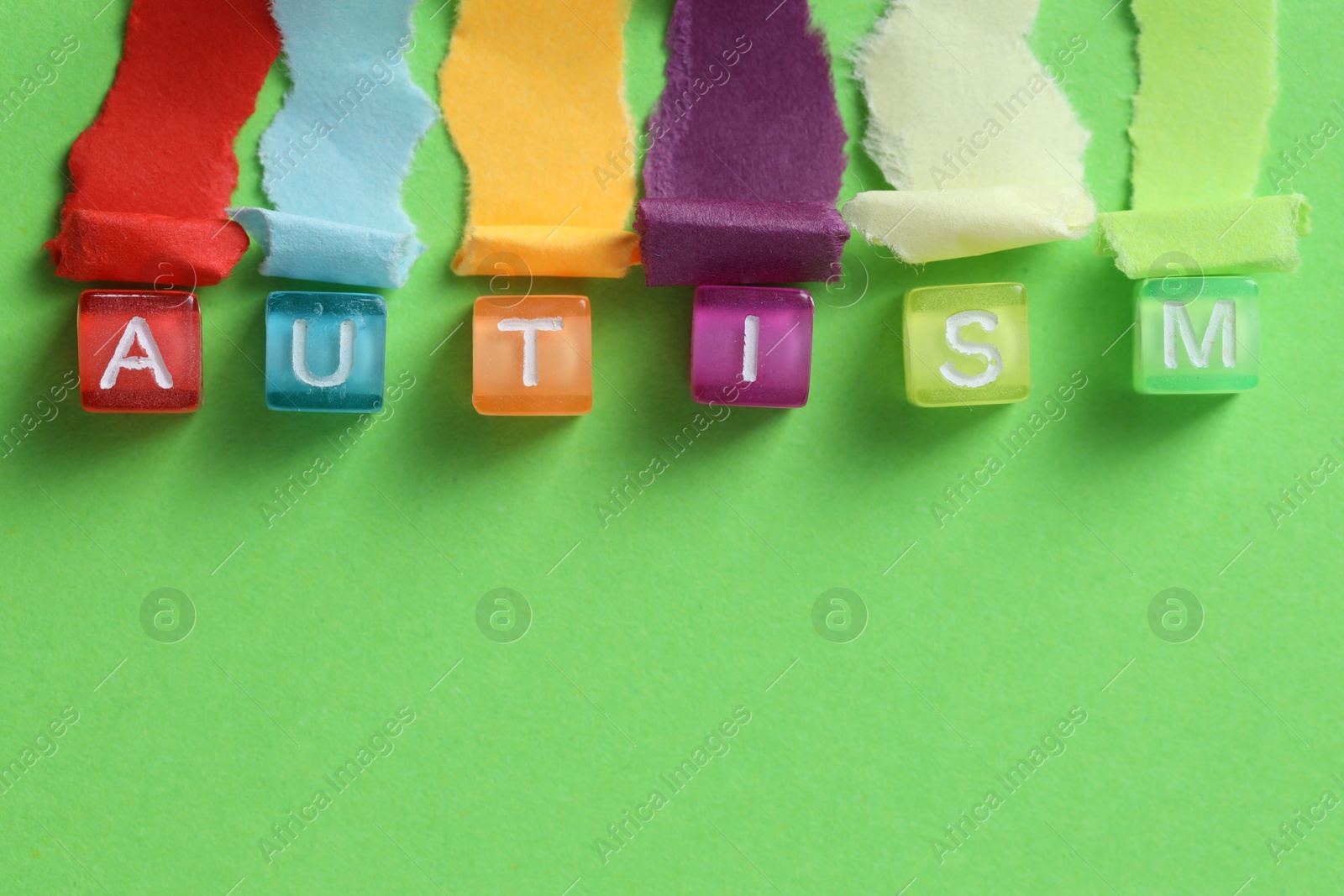 Photo of Word Autism made with cubes and cut colorful paper on green background, flat lay. Space for text