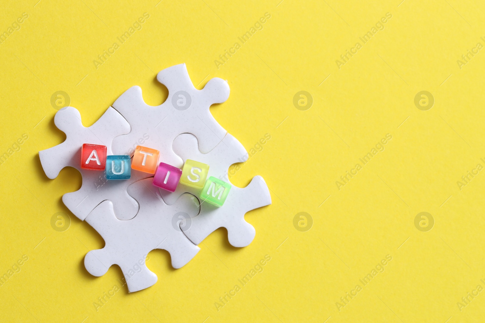 Photo of Word Autism made with colorful cubes and puzzle pieces on yellow background, flat lay. Space for text