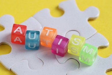 Photo of Word Autism made with colorful cubes and puzzle pieces on yellow background, closeup