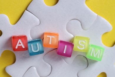 Photo of Word Autism made with colorful cubes and puzzle pieces on yellow background, flat lay