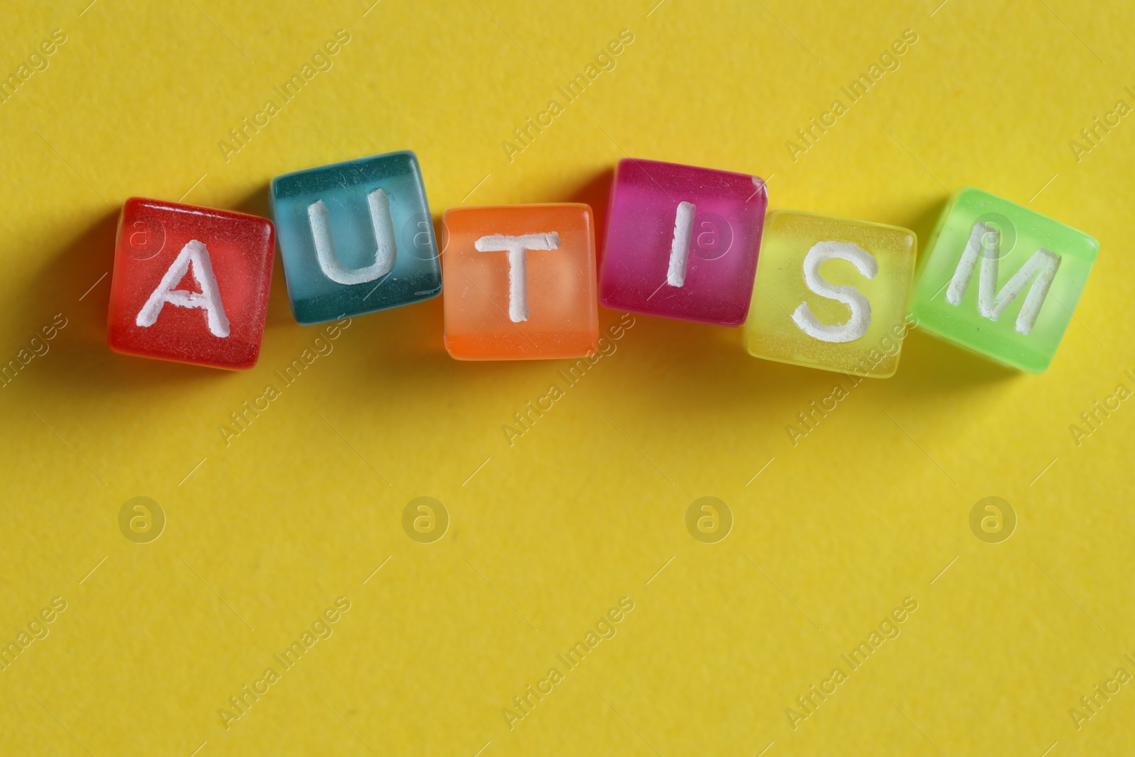 Photo of Word Autism made with colorful cubes on yellow background, top view. Space for text