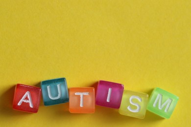 Photo of Word Autism made with colorful cubes on yellow background, top view. Space for text