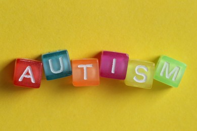 Photo of Word Autism made with colorful cubes on yellow background, top view