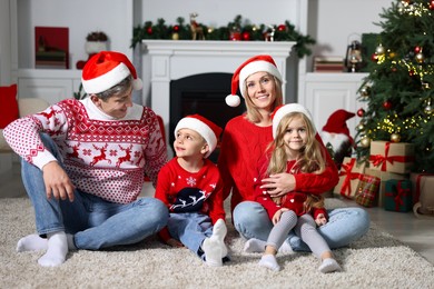 Photo of Lovely family in Christmas sweaters and Santa hats at home