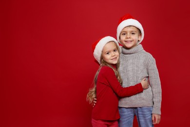 Photo of Cute little children in Santa hats on red background, space for text. Christmas season