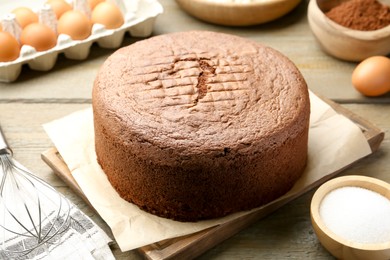 Photo of Tasty chocolate sponge cake and ingredients on wooden table, closeup