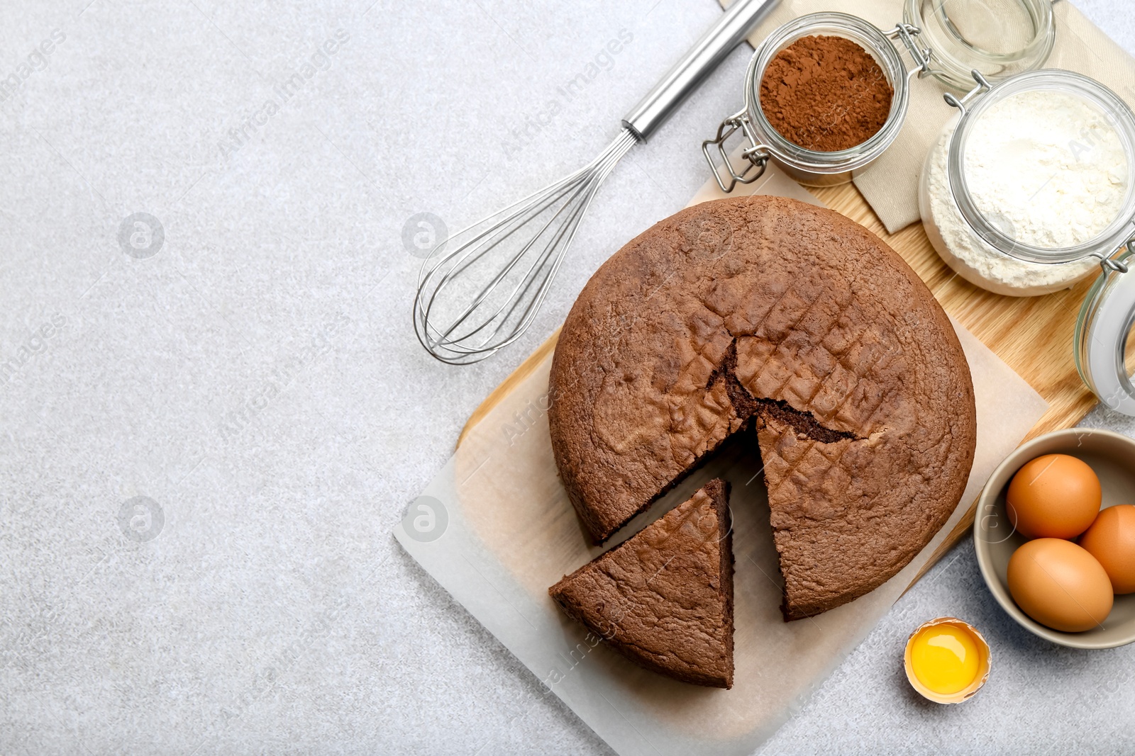 Photo of Cut chocolate sponge cake, whisk and ingredients on light table, flat lay. Space for text