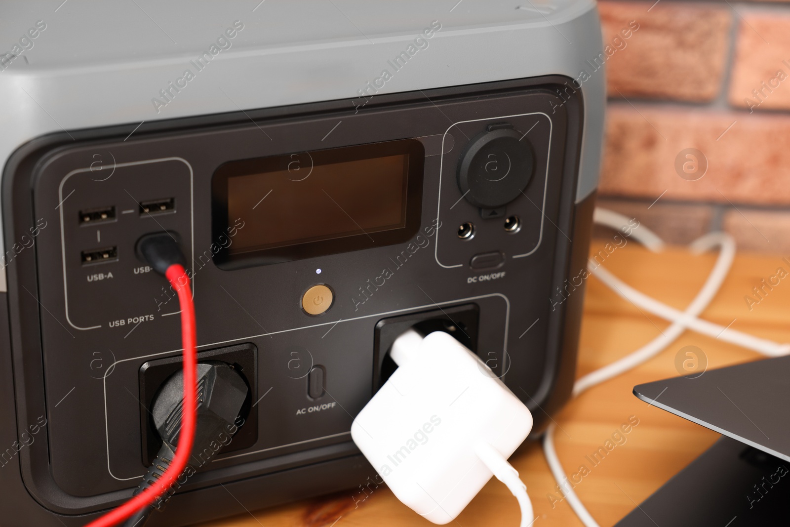 Photo of Laptop charging from portable power station on wooden desk indoors, closeup