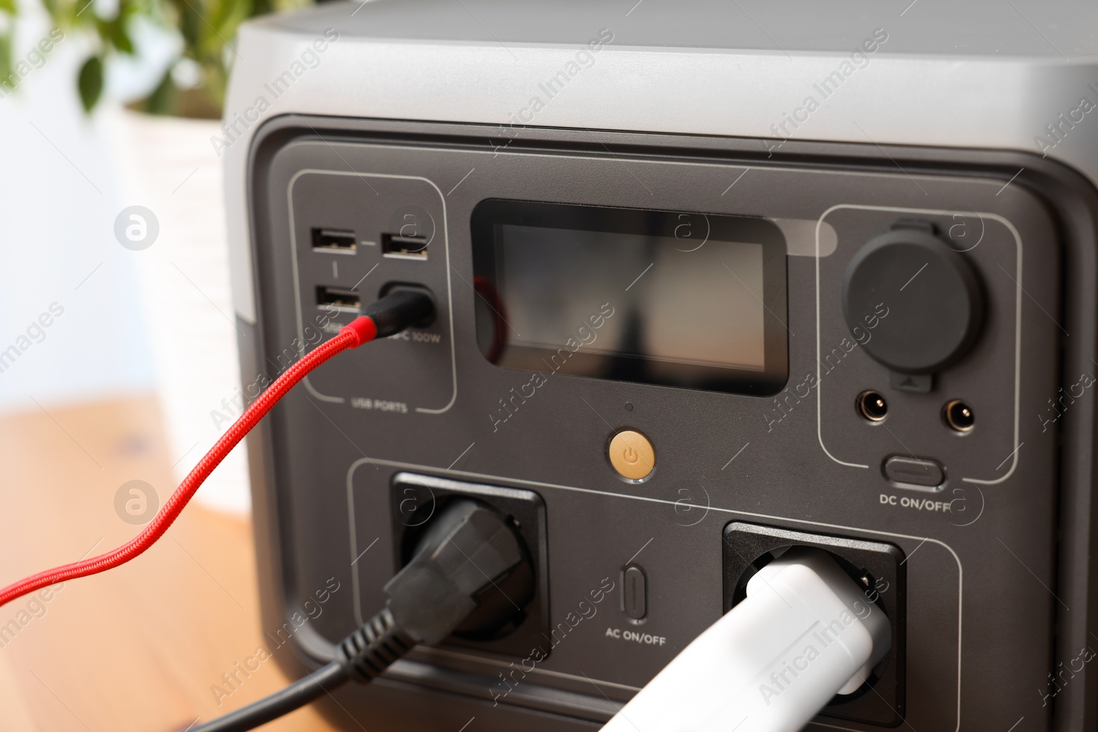 Photo of Portable power station with chargers on wooden desk indoors, closeup