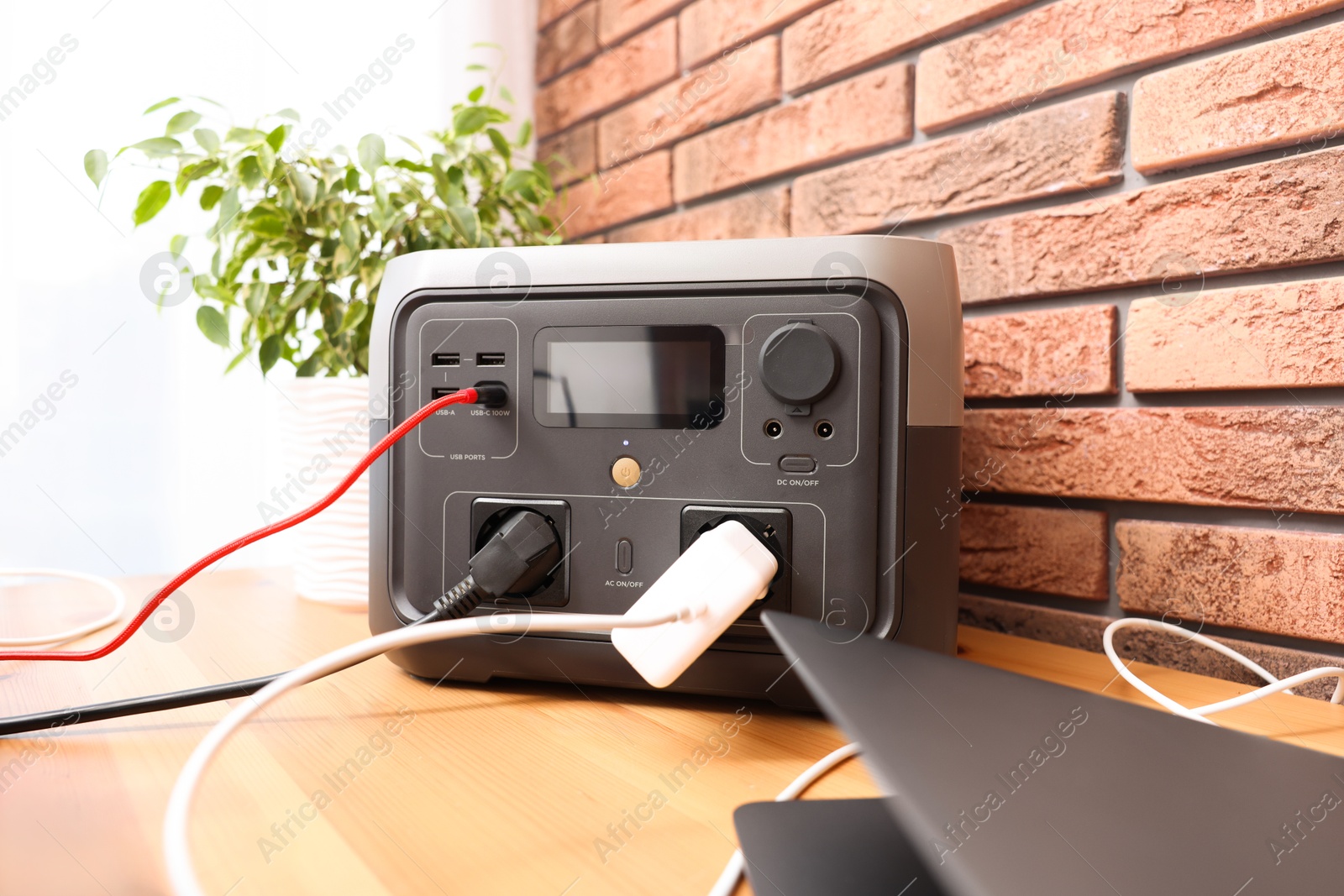 Photo of Laptop charging from portable power station on wooden desk indoors