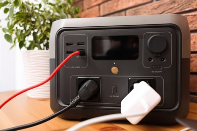 Photo of Portable power station with chargers on wooden desk indoors, closeup