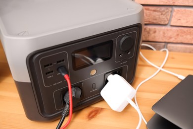 Photo of Laptop charging from portable power station on wooden desk indoors, closeup