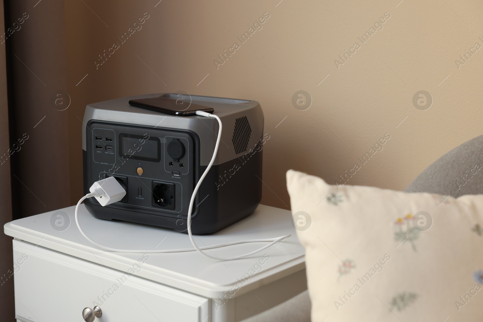 Photo of Smartphone charging from portable power station on nightstand indoors