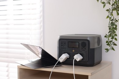 Photo of Laptop charging from portable power station on wooden table indoors