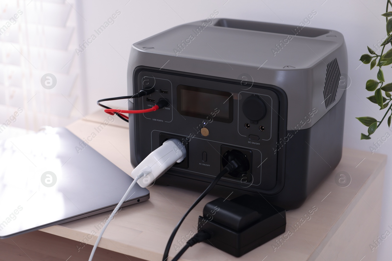 Photo of Laptop charging from portable power station on wooden table indoors