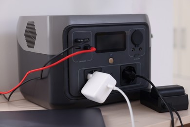 Photo of Laptop charging from portable power station on wooden table indoors