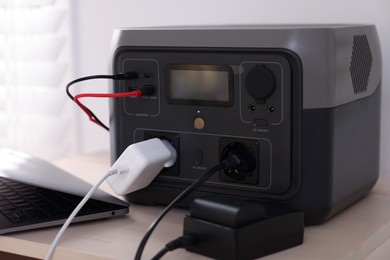 Photo of Laptop charging from portable power station on wooden table indoors