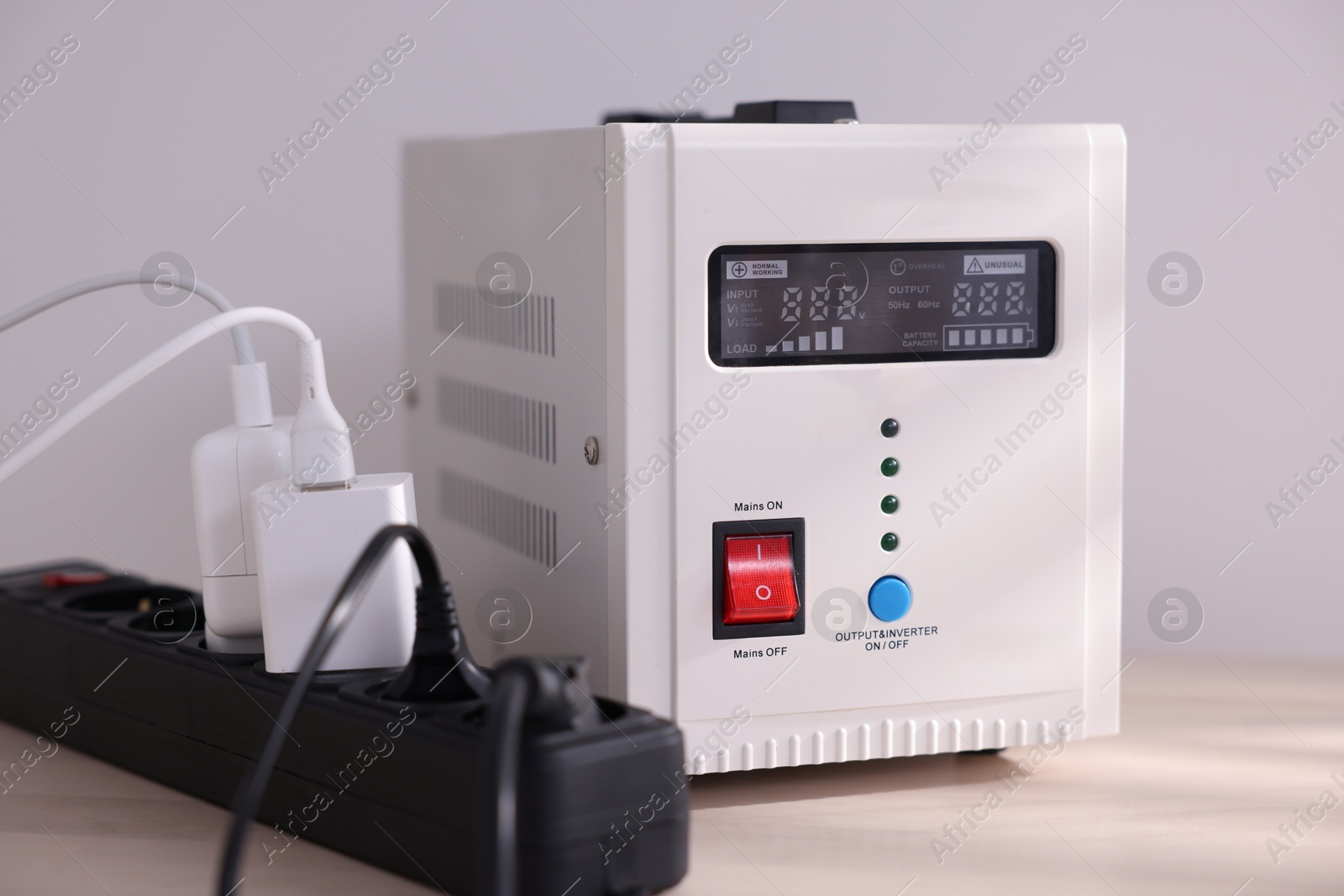 Photo of Portable power station and multi-socket extension board with chargers on table indoors, closeup