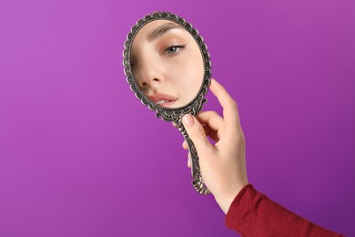 Image of Beautiful woman looking in handheld mirror on purple background, closeup