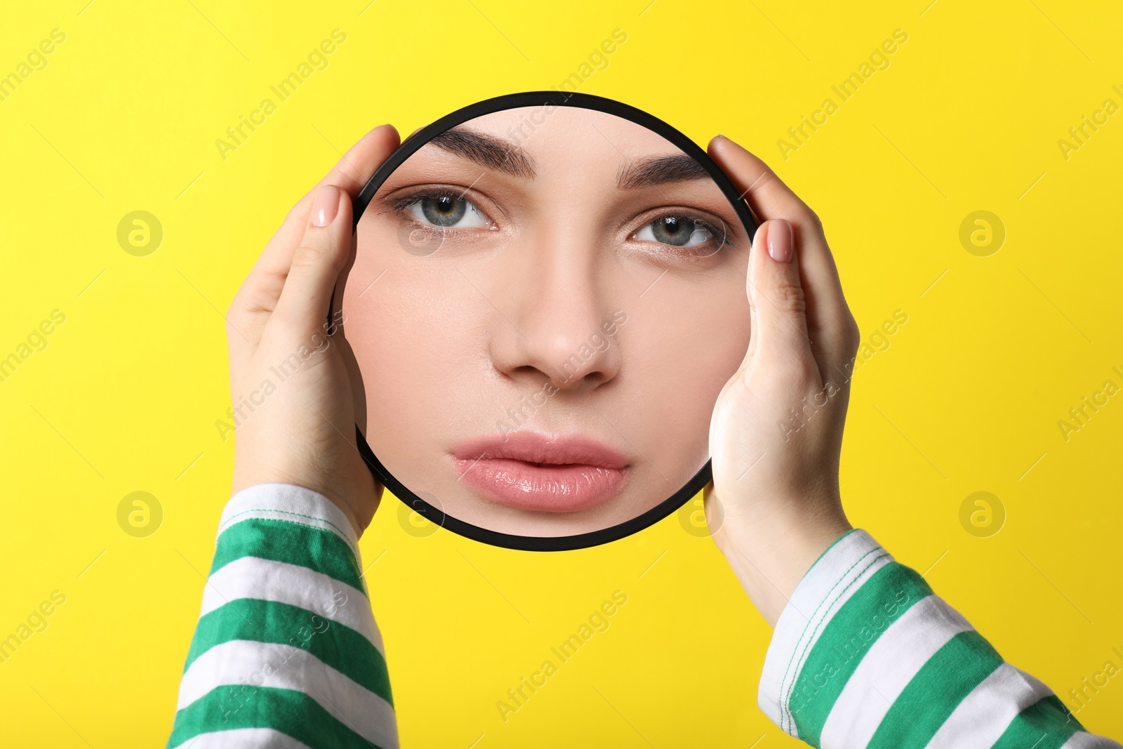 Image of Beautiful woman looking in small round mirror on yellow background, closeup