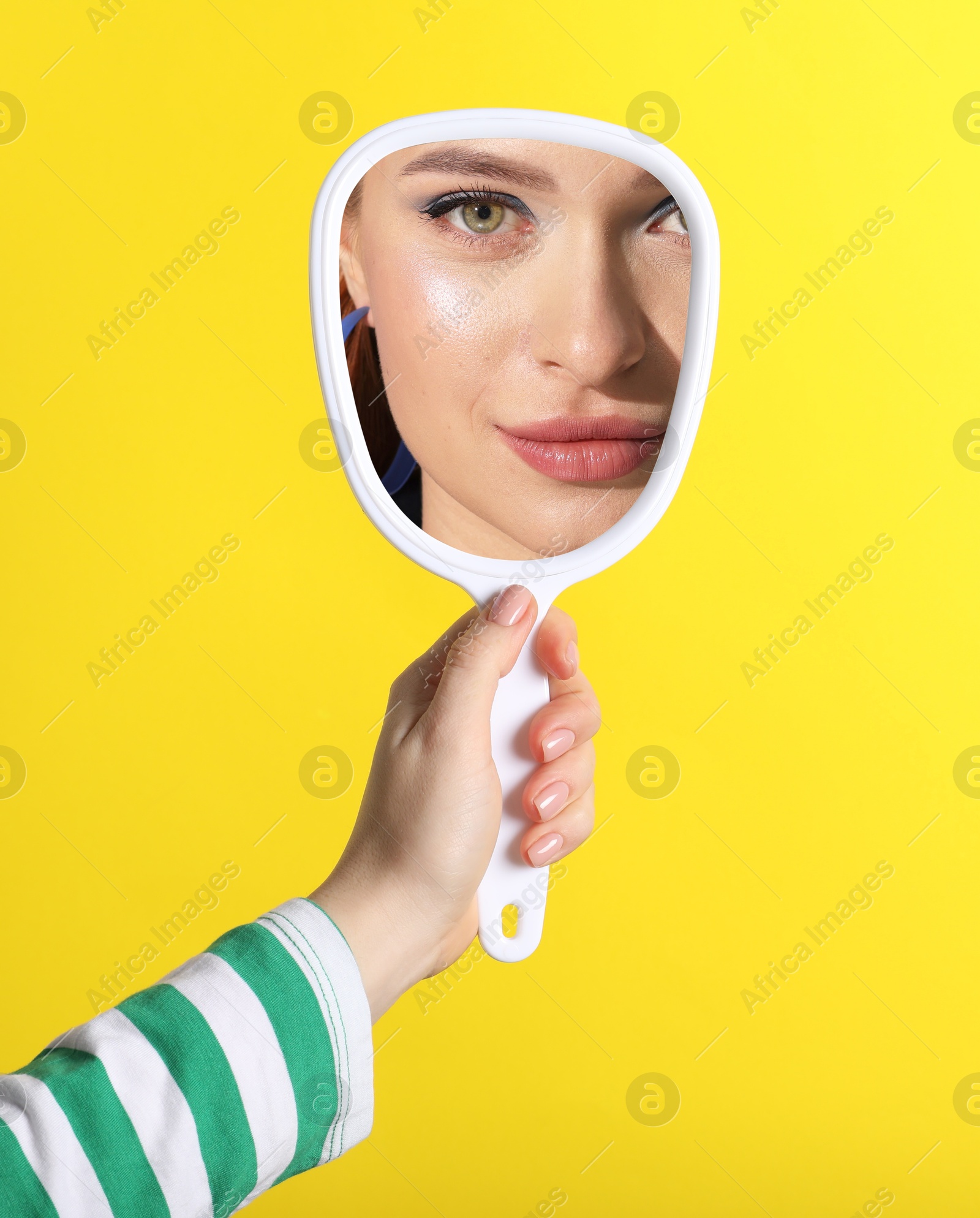 Image of Beautiful woman looking in handheld mirror on yellow background, closeup