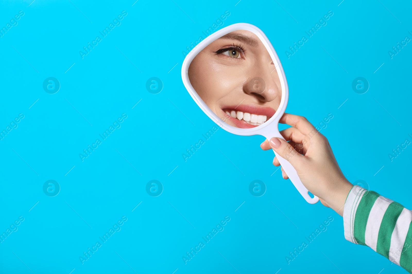 Image of Beautiful woman looking in handheld mirror on light blue background, closeup. Space for text