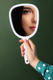 Image of Beautiful woman looking in handheld mirror on dark green background, closeup