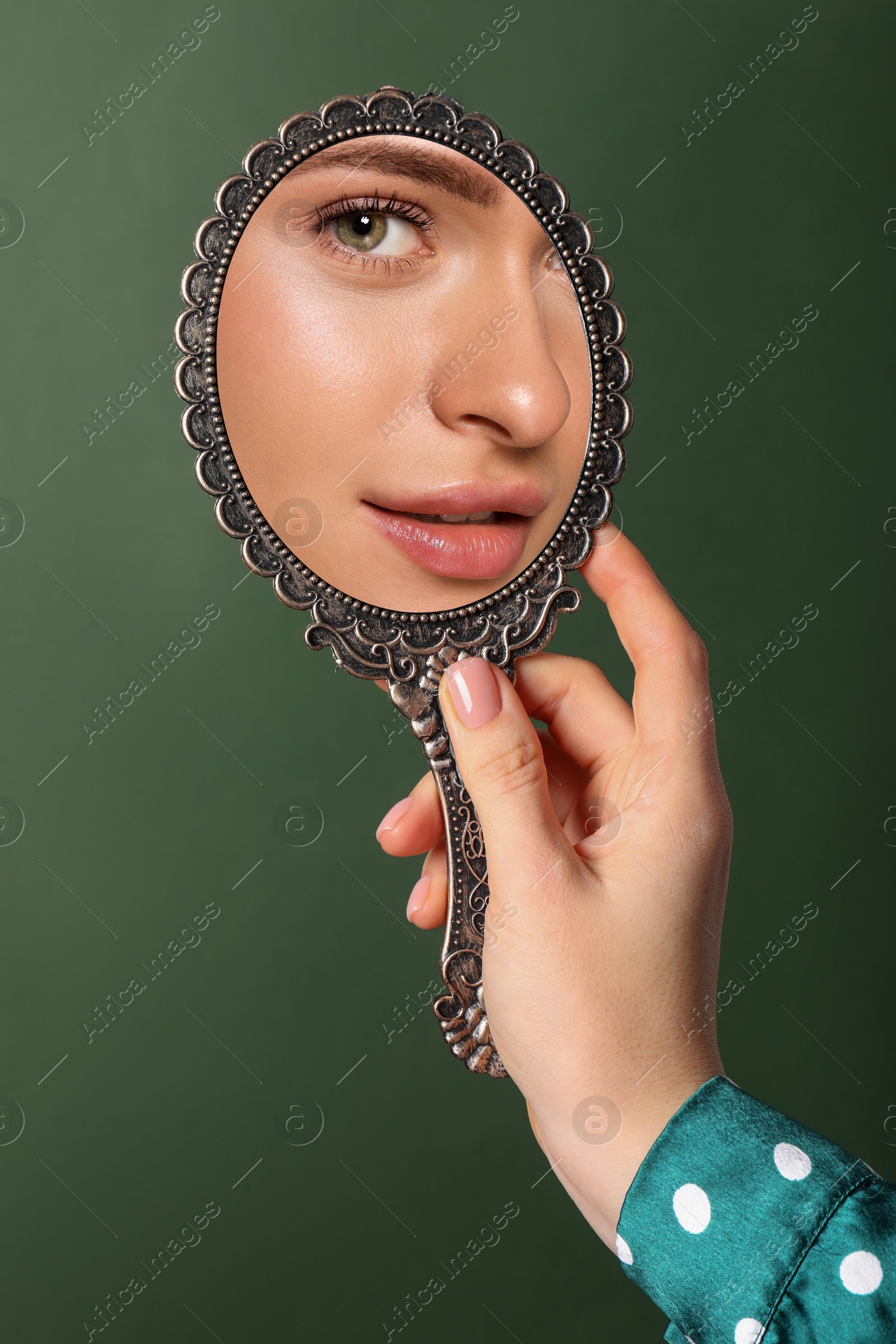 Image of Beautiful woman looking in handheld mirror on dark green background, closeup