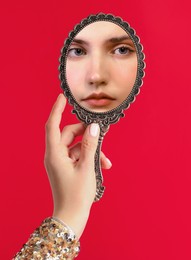 Image of Beautiful woman looking in handheld mirror on red background, closeup