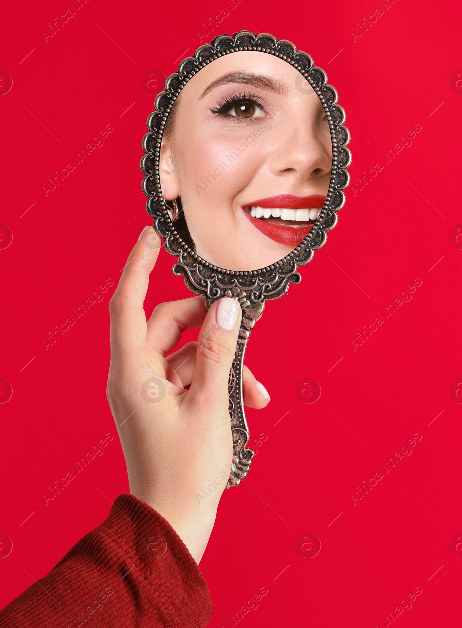 Image of Beautiful woman looking in handheld mirror on red background, closeup