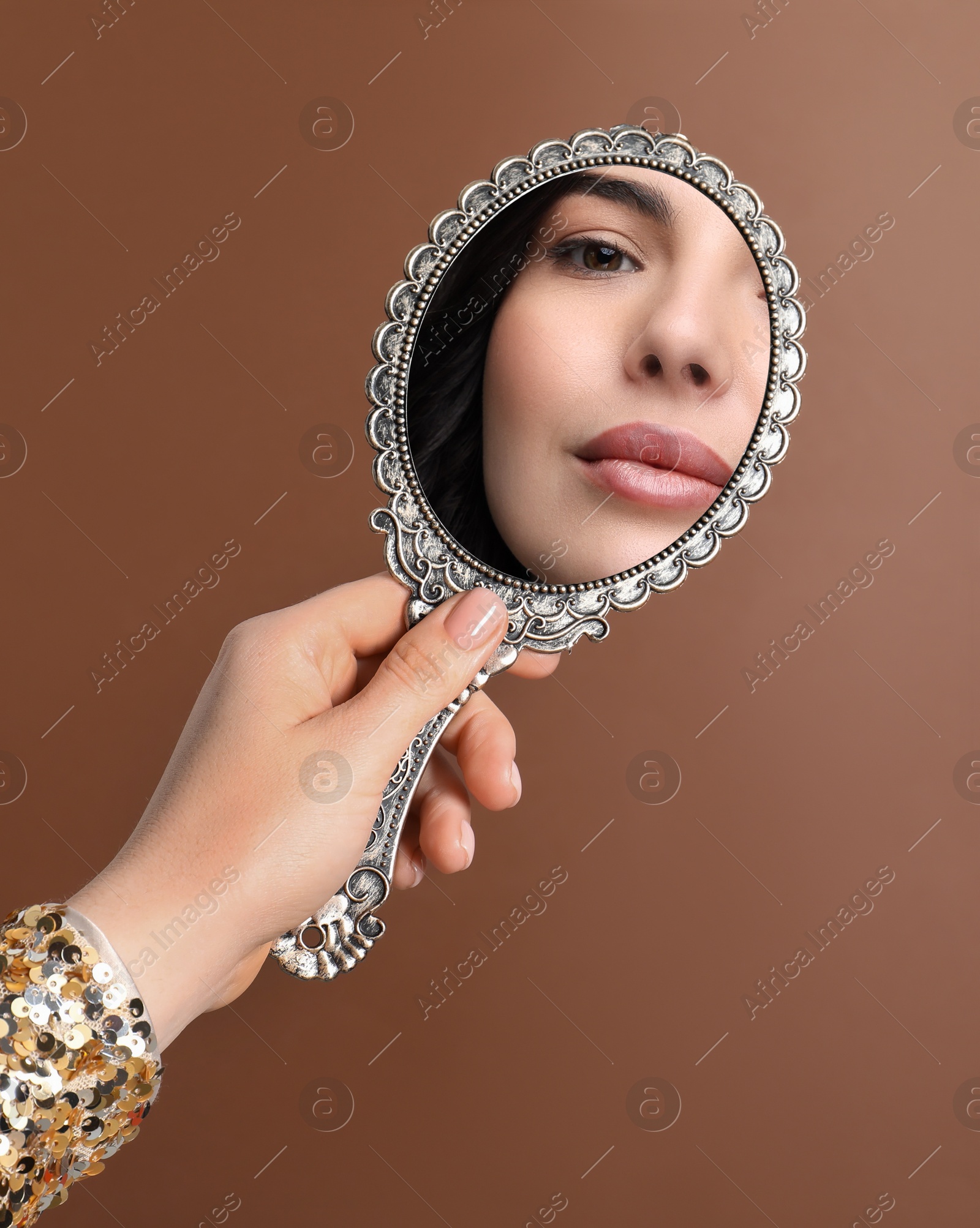 Image of Beautiful woman looking in handheld mirror on brown background, closeup