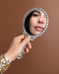 Image of Beautiful woman looking in handheld mirror on brown background, closeup