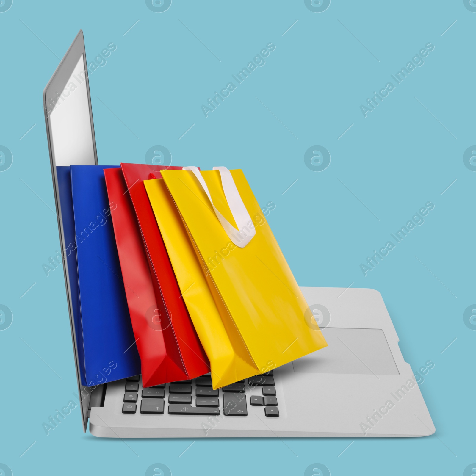 Image of Laptop with shopping bags on light blue background. Concept of online shopping, purchase via internet