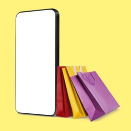 Image of Mobile phone and shopping bags on yellow background. Concept of online shopping, purchase via internet