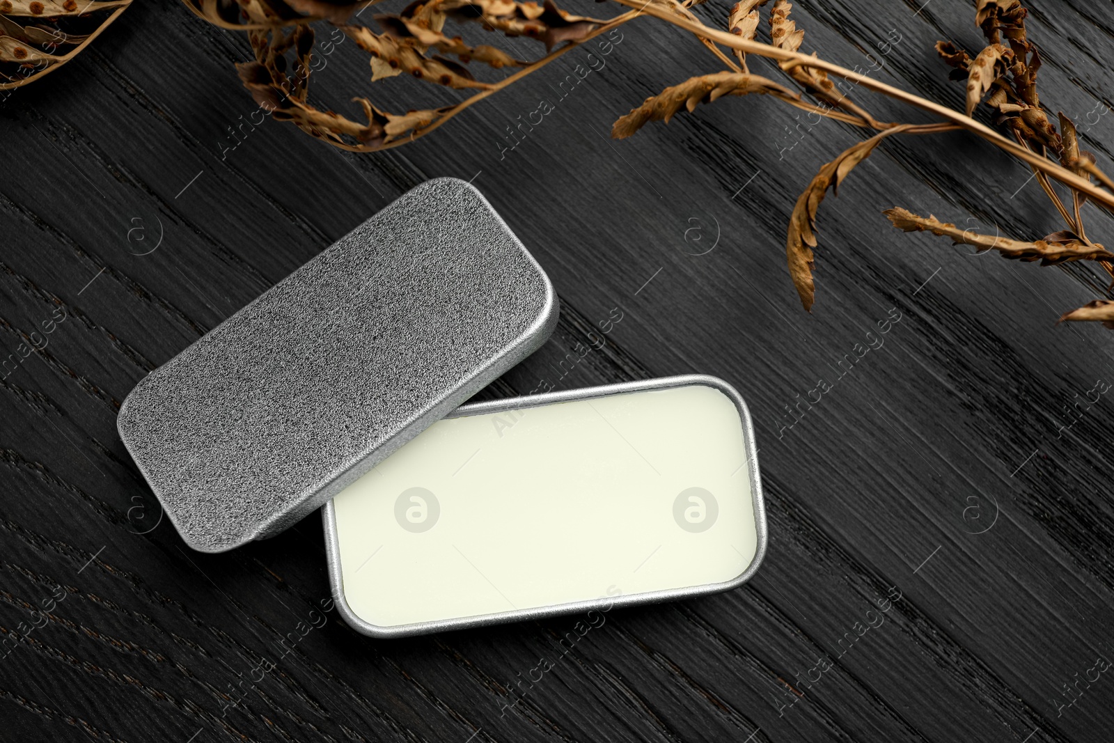 Photo of Natural solid perfume and dry branch on black wooden table, flat lay