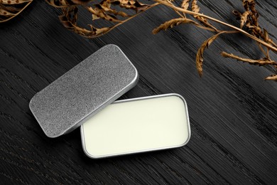 Photo of Natural solid perfume and dry branch on black wooden table, flat lay