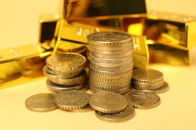 Photo of Gold bars and coins on pale yellow background, closeup