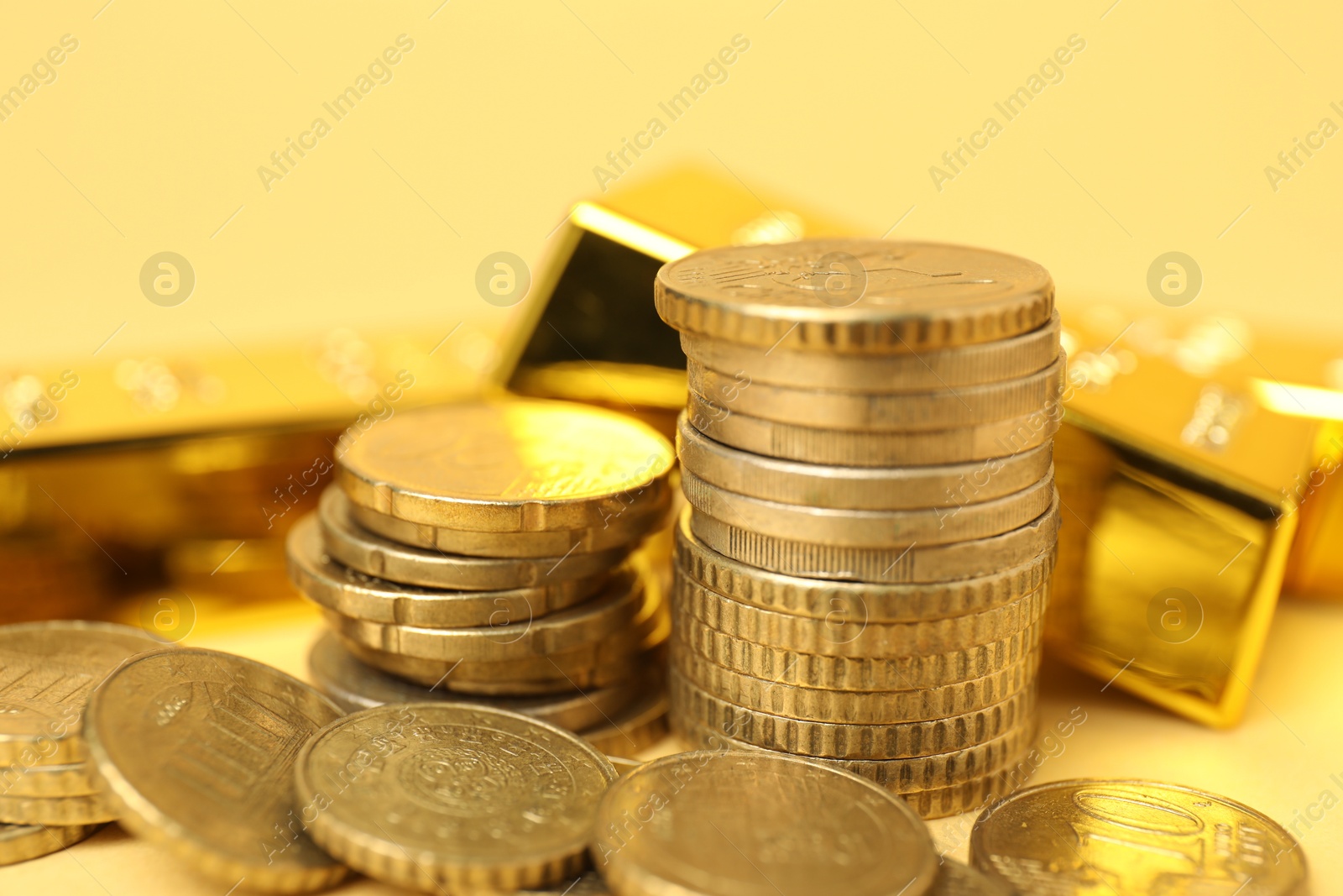 Photo of Gold bars and coins on pale yellow background, closeup