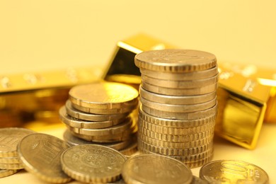 Photo of Gold bars and coins on pale yellow background, closeup